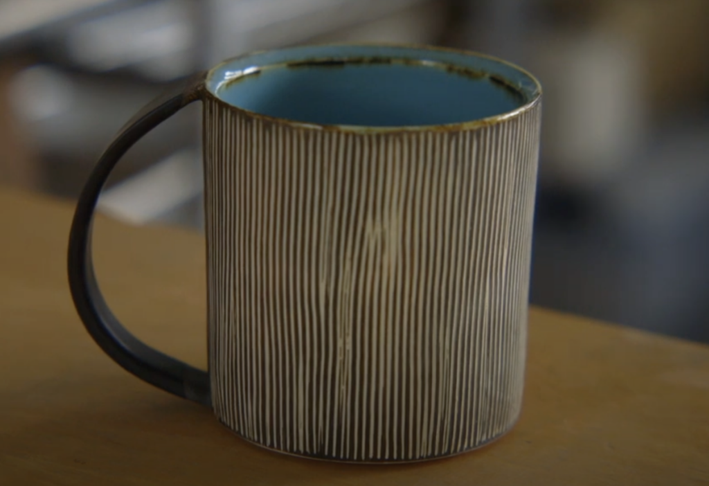 Still from student film "Balancing" with a rustic cup with vertical stripes sitting on a table