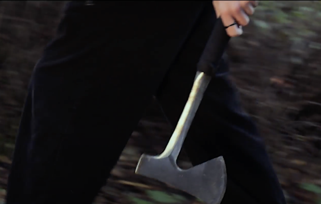 Still from student film "Leave no Trace" with a  person holding an axe and walking