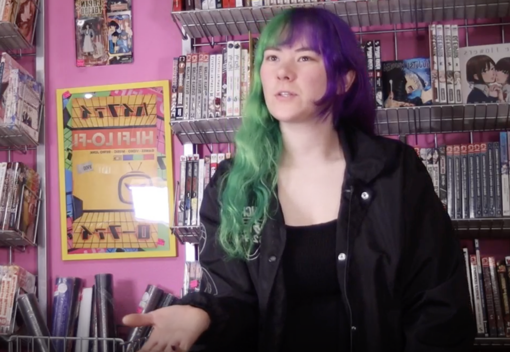 Still from student film "Seattle Music" featuring a person in a music store with a pink wall in the background and many posters